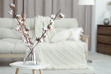 Photo of Branches with white fluffy cotton flowers on coffee table in cozy room, space for text. Interior design