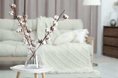 Branches with white fluffy cotton flowers on coffee table in cozy room, space for text. Interior design