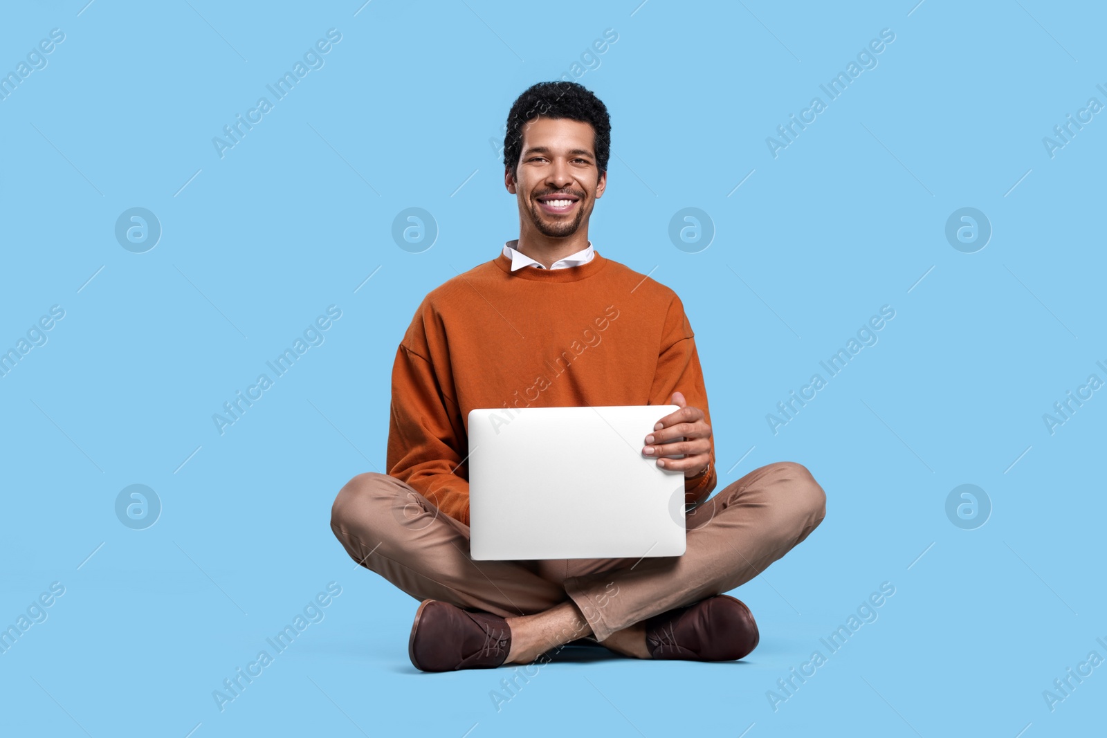 Photo of Happy man with laptop sitting on light blue background