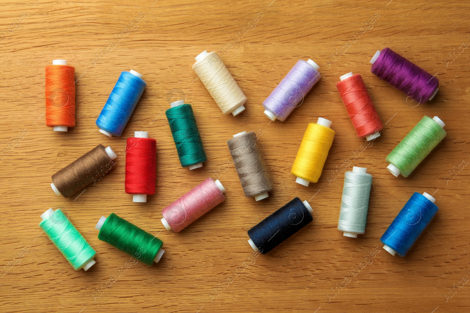 Photo of Many colorful sewing threads on wooden table, flat lay