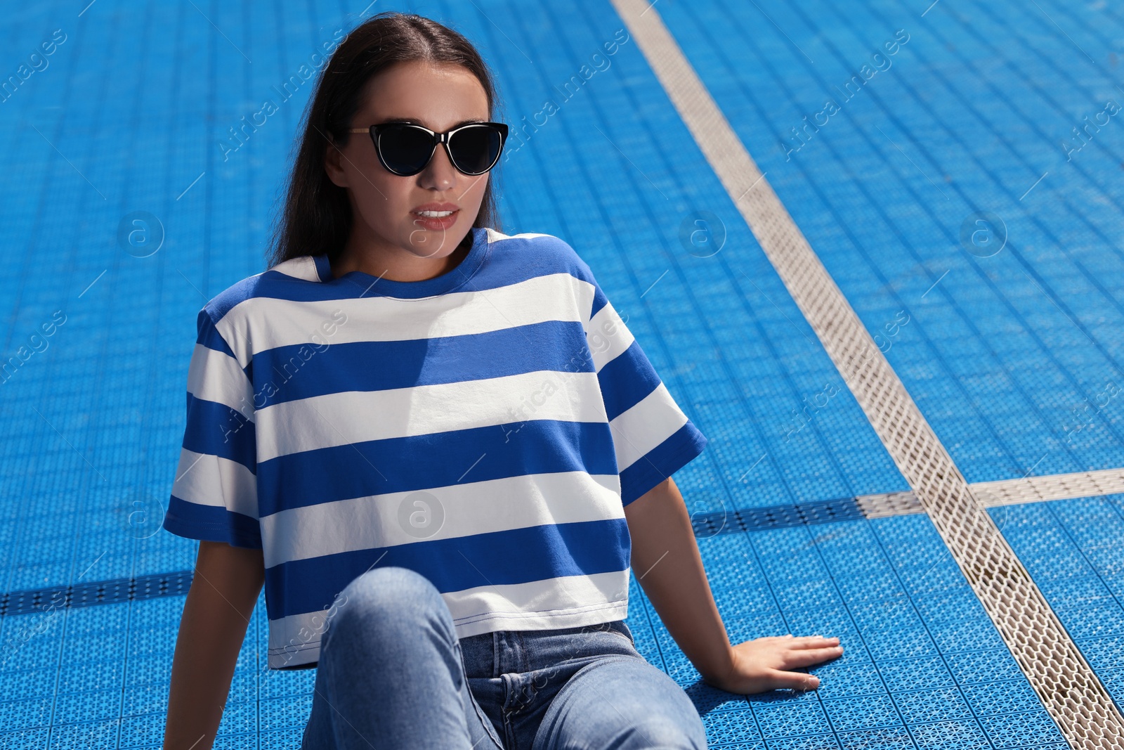 Photo of Beautiful woman in sunglasses on blue floor covering outdoors, space for text