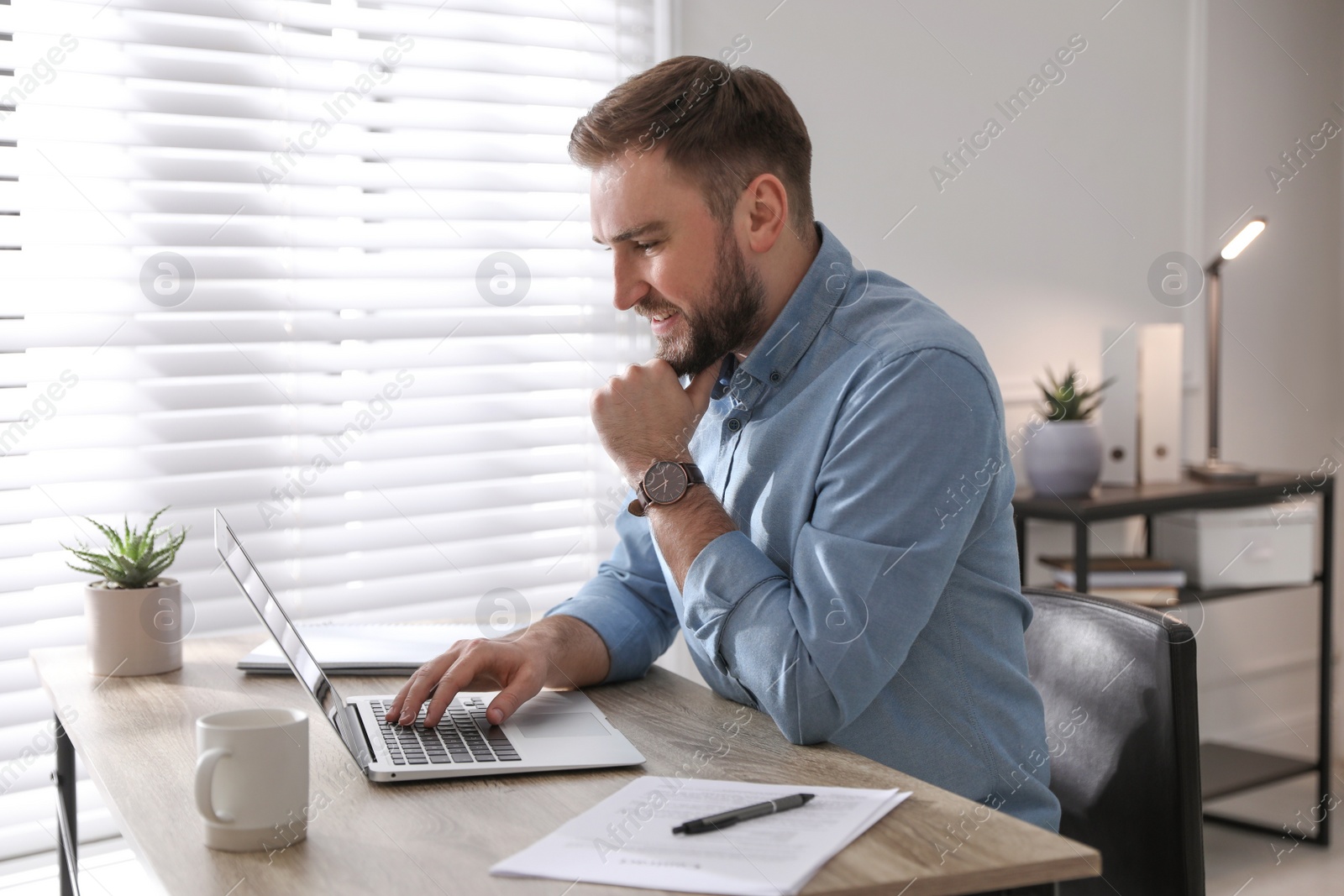 Photo of Young man working on laptop at table in office