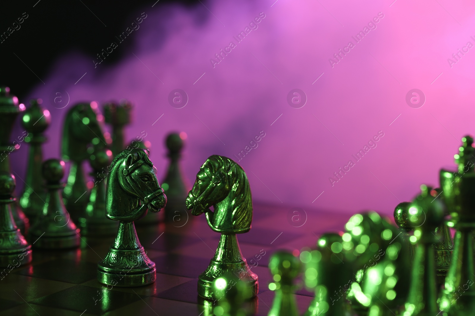 Photo of Two knights and other chess pieces on checkerboard in color light, selective focus. Space for text
