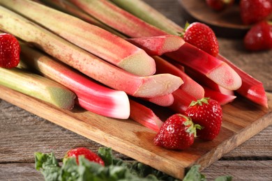 Photo of Cut fresh rhubarb stalks and strawberries on wooden table, closeup