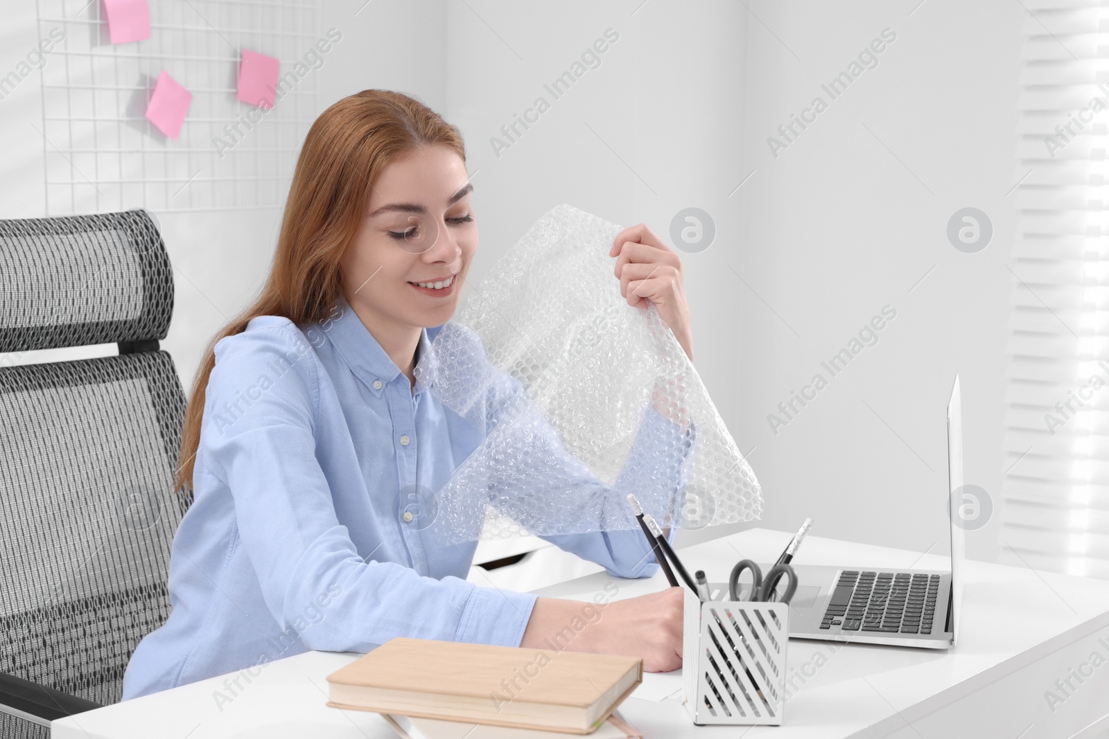 Photo of Woman popping bubble wrap at desk in office, space for text. Stress relief