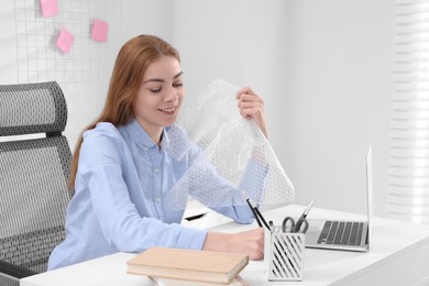 Photo of Woman popping bubble wrap at desk in office, space for text. Stress relief