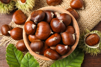 Photo of Fresh sweet edible chestnuts on brown wooden table, flat lay