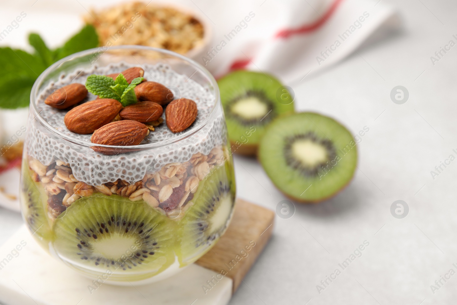 Photo of Delicious dessert with kiwi, chia seeds and almonds on light table, closeup. Space for text