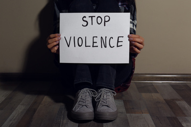 Photo of Young woman with sign STOP VIOLENCE near beige wall, closeup