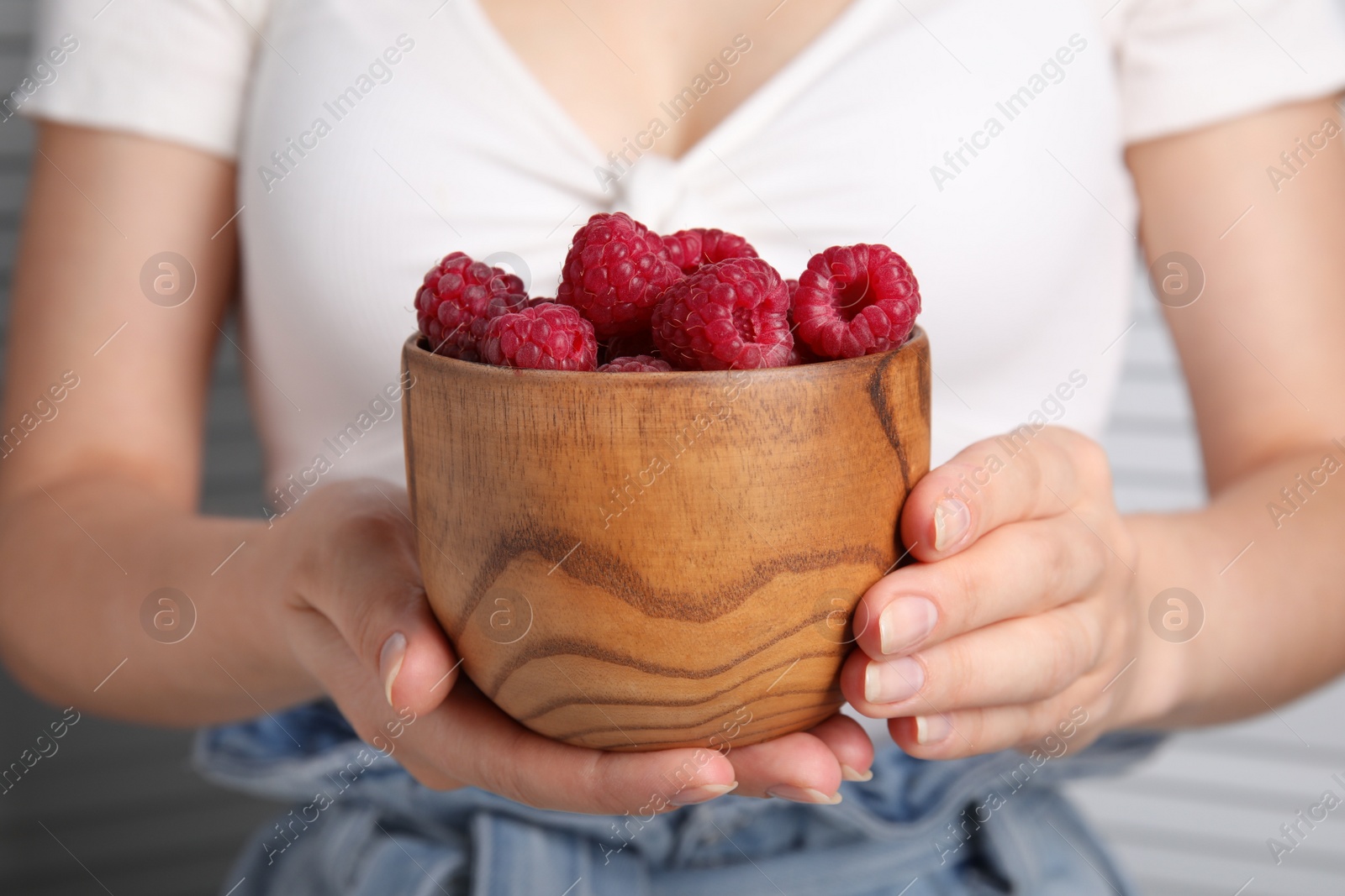 Photo of Woman holding wooden bowl of fresh raspberries, closeup