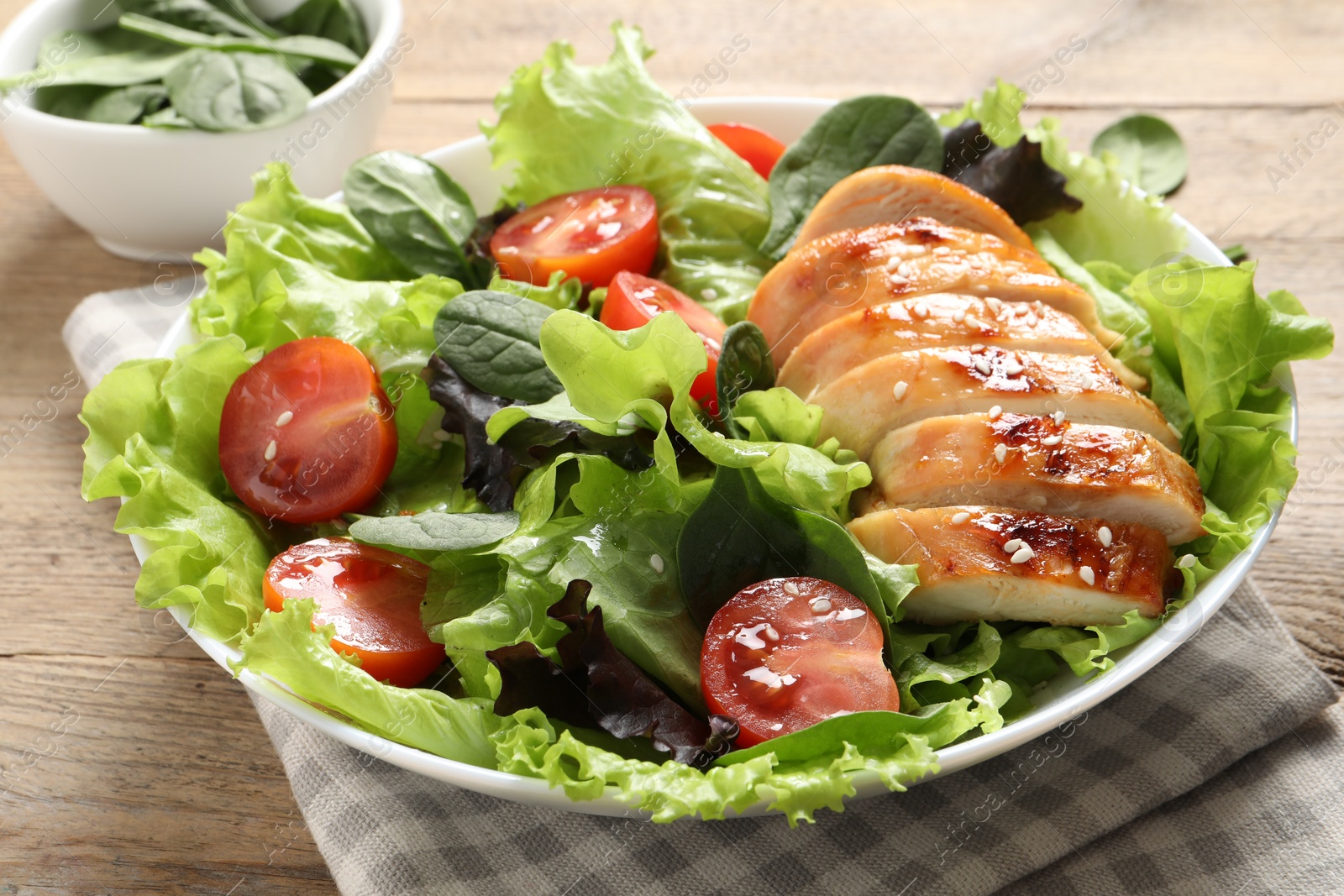 Photo of Delicious salad with chicken, cherry tomato and spinach on wooden table, closeup
