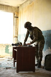 Military mission. Soldier in uniform using laptop at table inside abandoned building