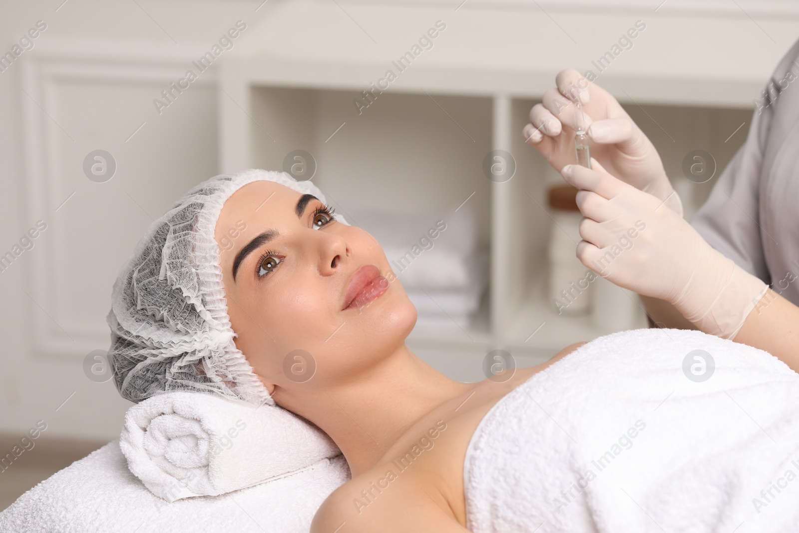 Photo of Professional cosmetologist holding skincare ampoule while working with client in clinic, closeup