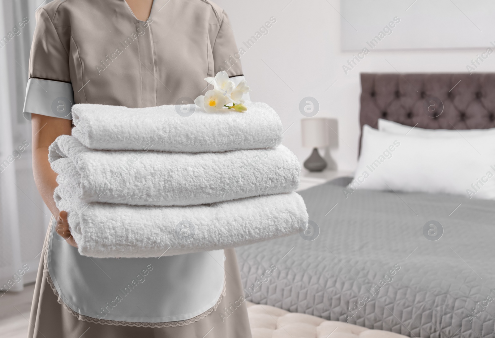 Photo of Maid holding fresh towels with flowers in hotel room, closeup