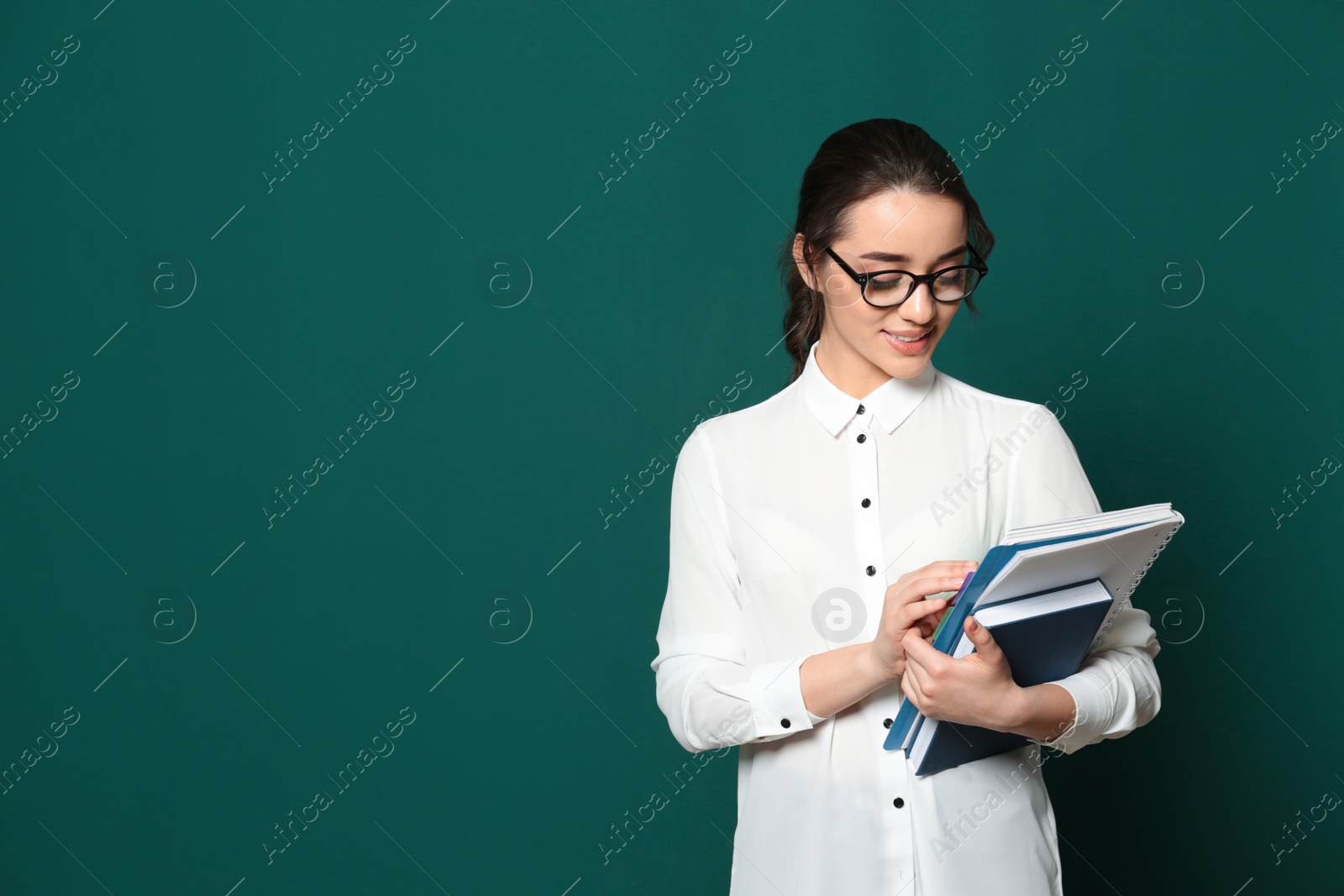 Photo of Portrait of beautiful young teacher with books near chalkboard, space for text