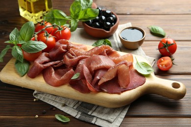 Photo of Board with delicious bresaola served with other snacks on wooden table