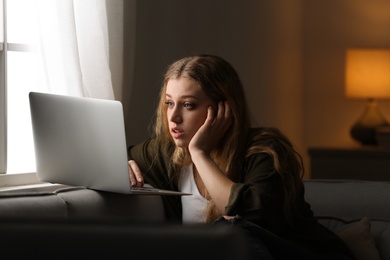 Photo of Young woman with laptop on sofa at home. Loneliness concept