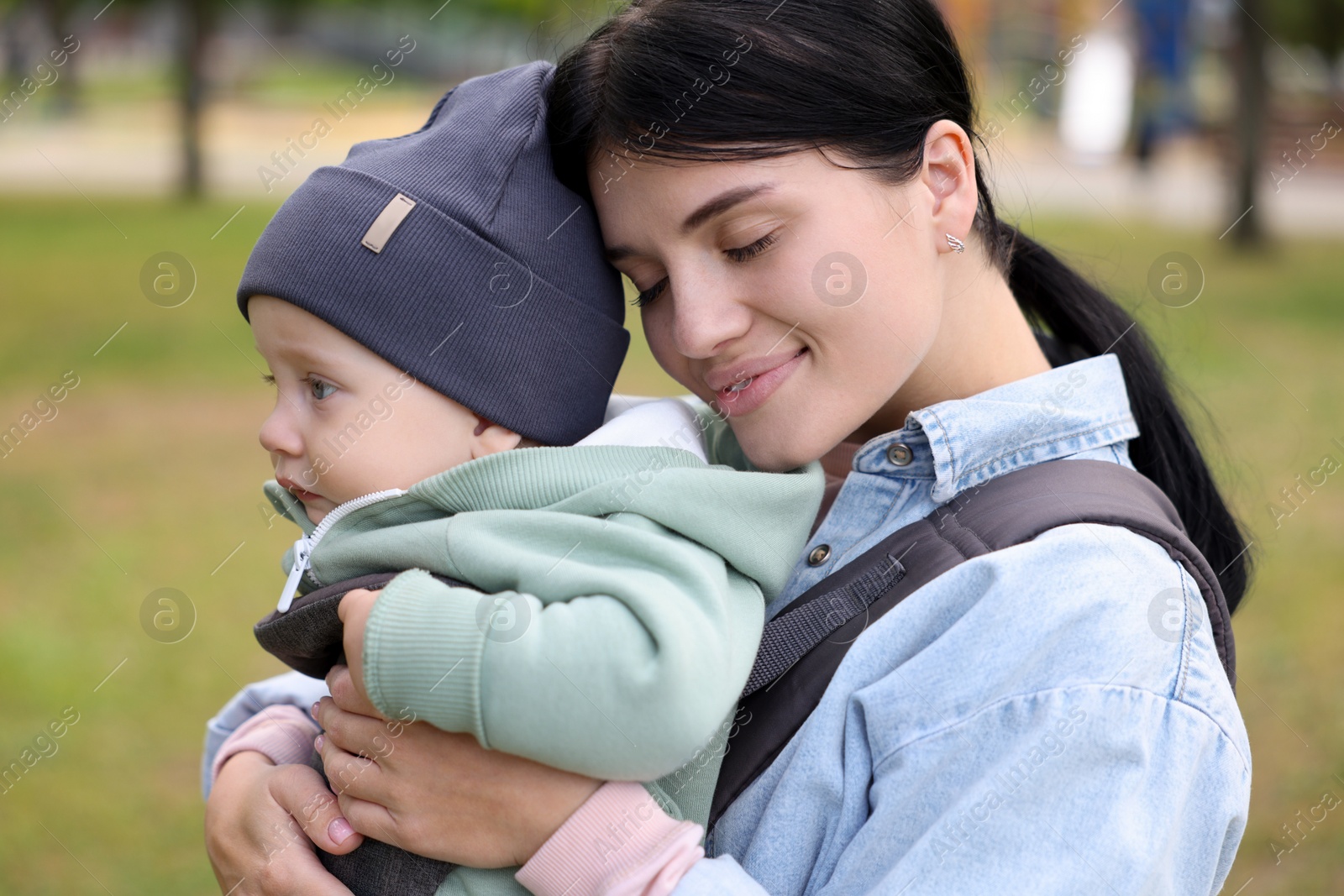 Photo of Mother holding her child in sling (baby carrier) in park