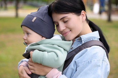 Mother holding her child in sling (baby carrier) in park