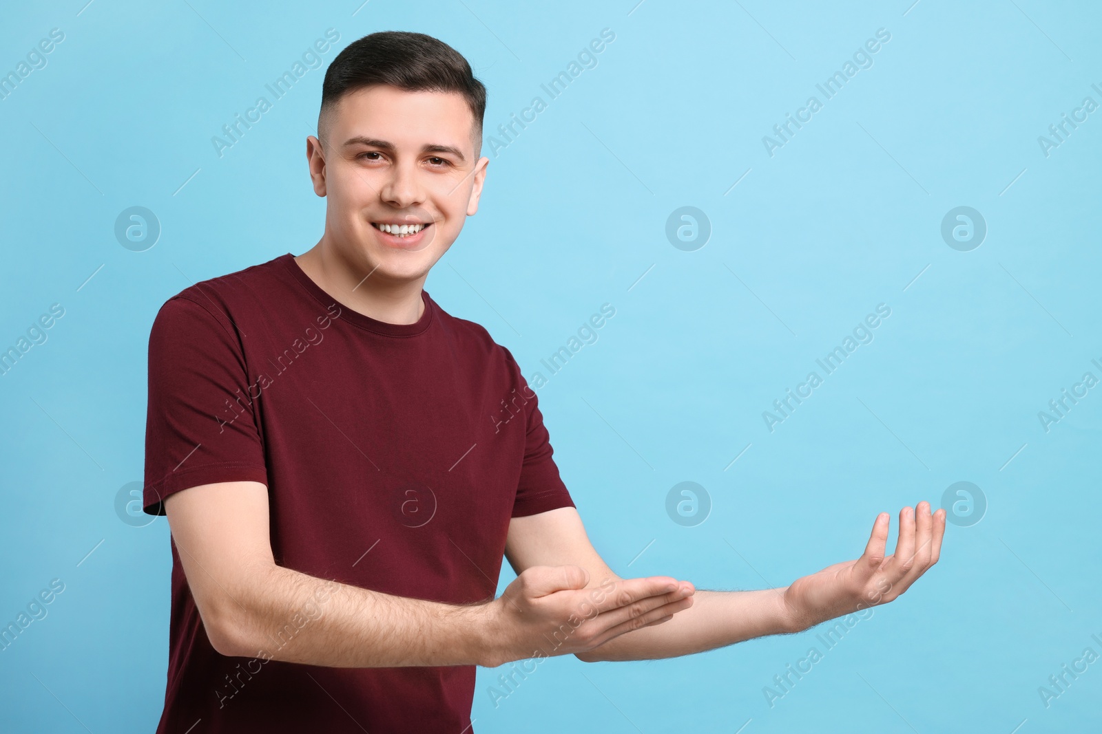 Photo of Handsome man inviting to come in against light blue background. Space for text