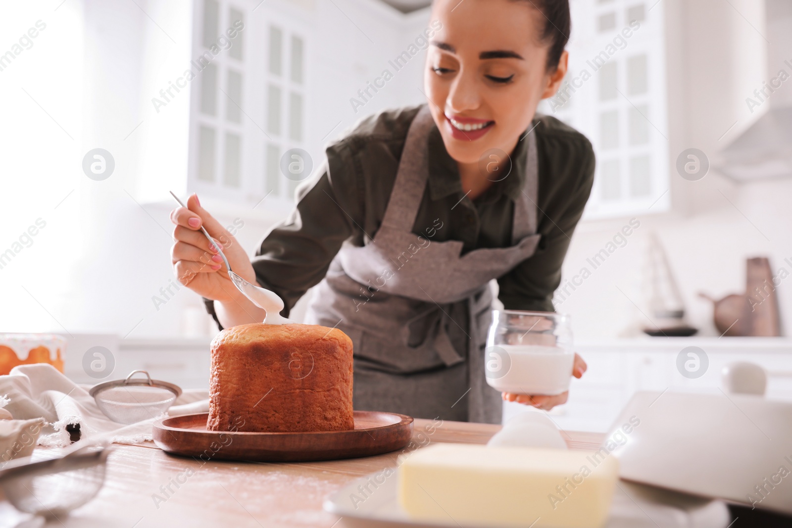 Photo of Young woman decorating traditional Easter cake with glaze in kitchen, focus on hand