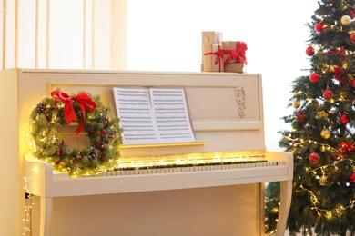 White piano with festive decor and music sheets near Christmas tree indoors