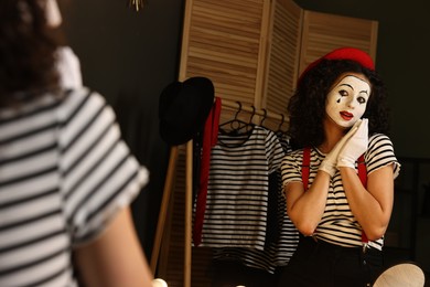 Photo of Young woman in mime costume posing near mirror indoors