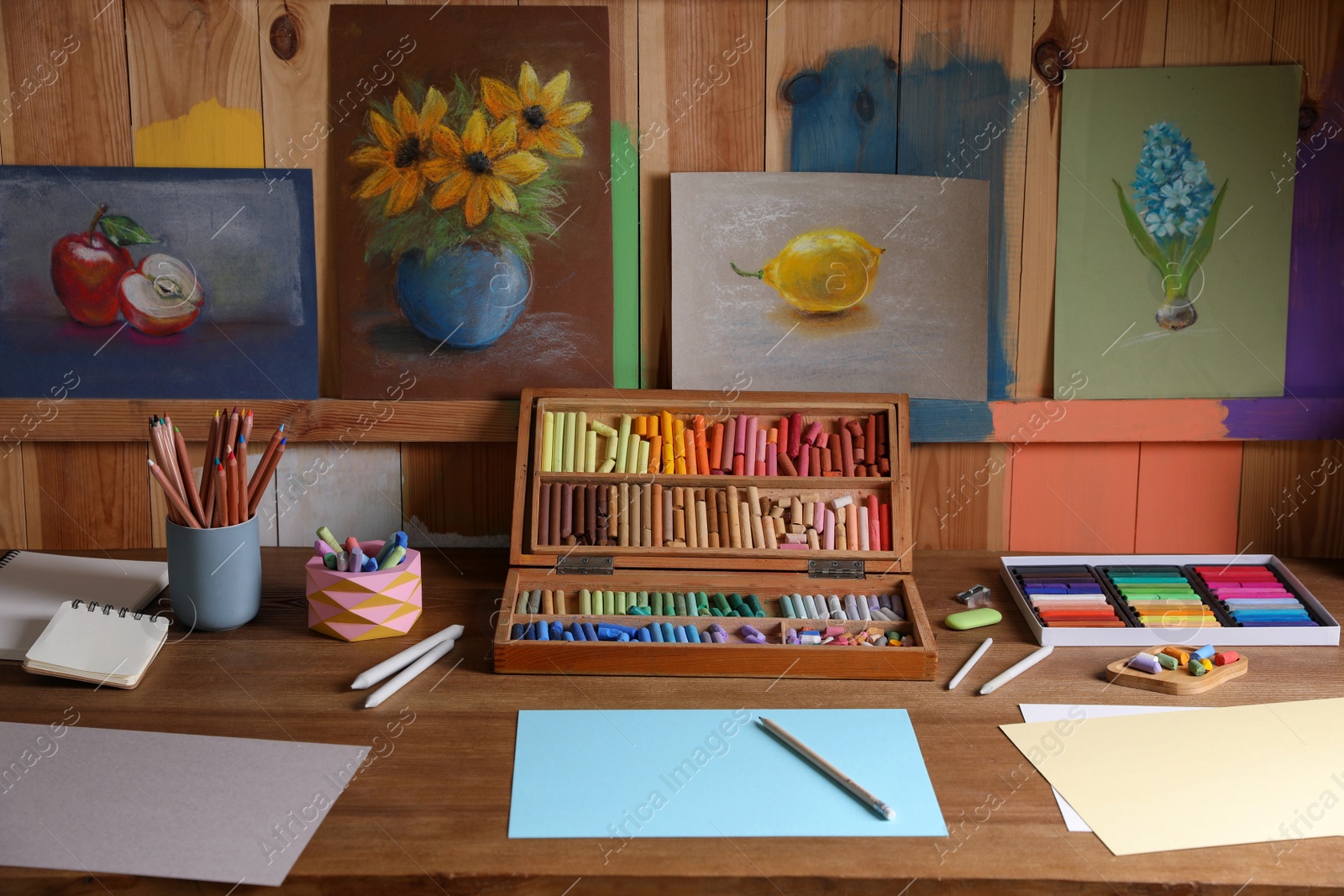 Photo of Blank sheets of paper, colorful chalk pastels and drawing pencils on wooden table indoors. Modern artist's workplace