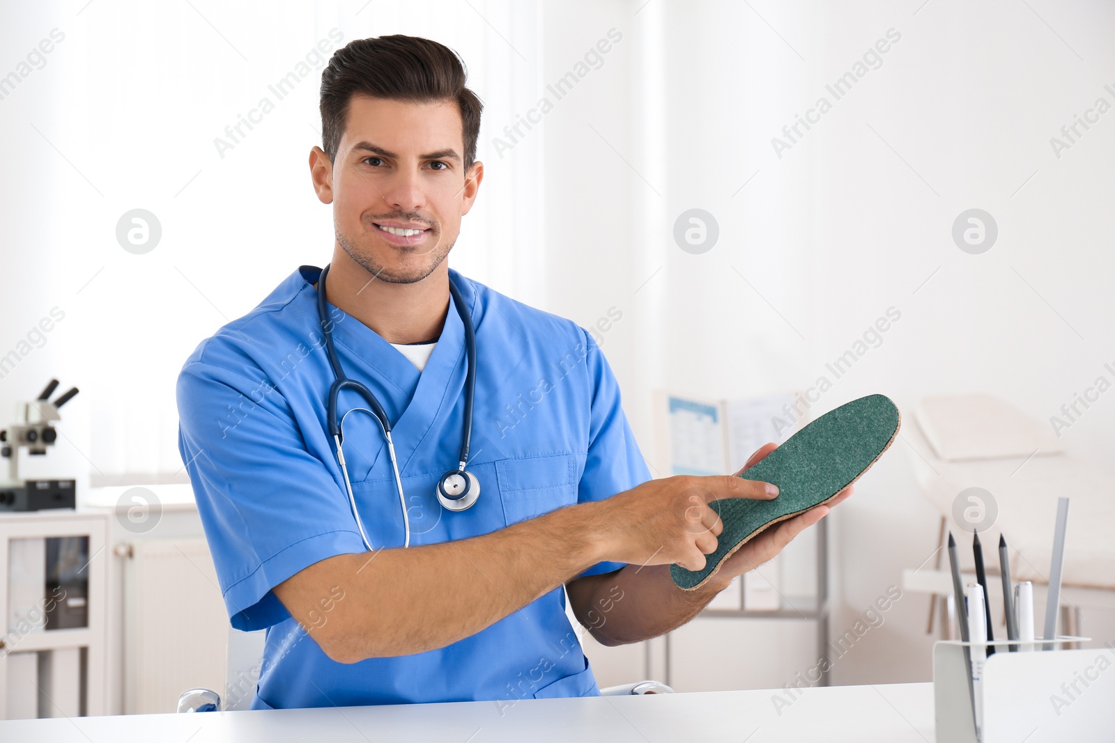 Photo of Handsome male orthopedist showing insole in clinic
