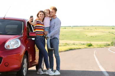 Photo of Happy young family taking selfie near car on road trip