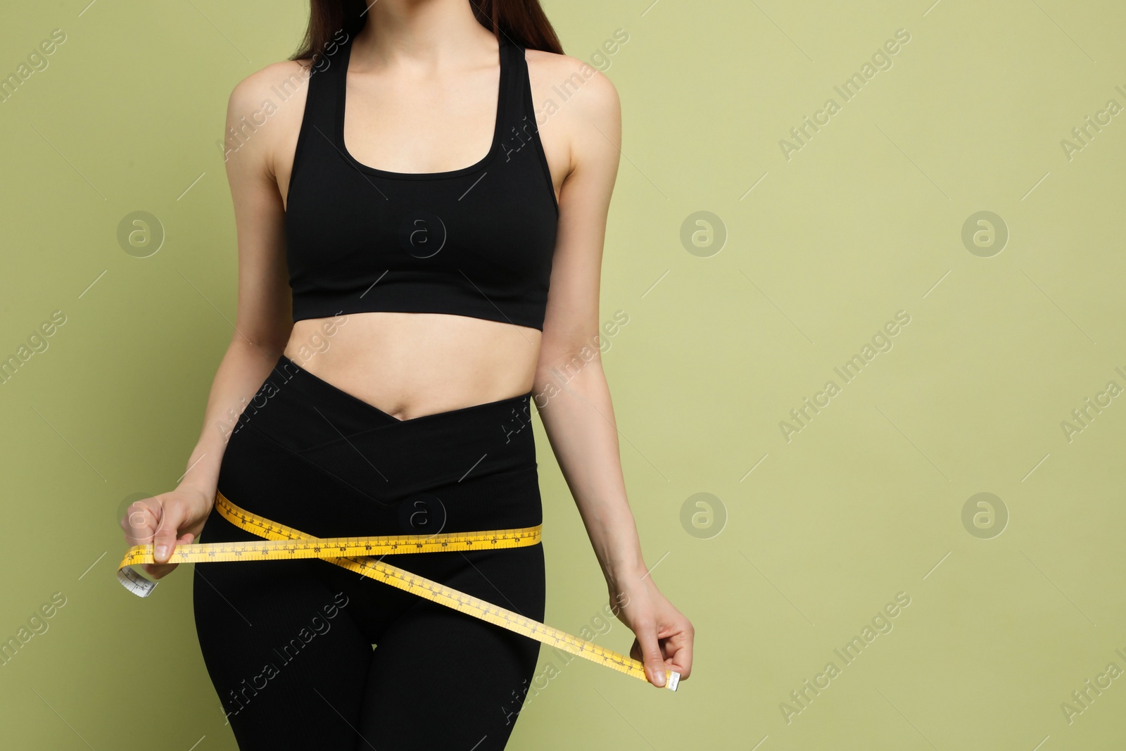 Photo of Woman with measuring tape showing her slim body on green background, closeup. Space for text