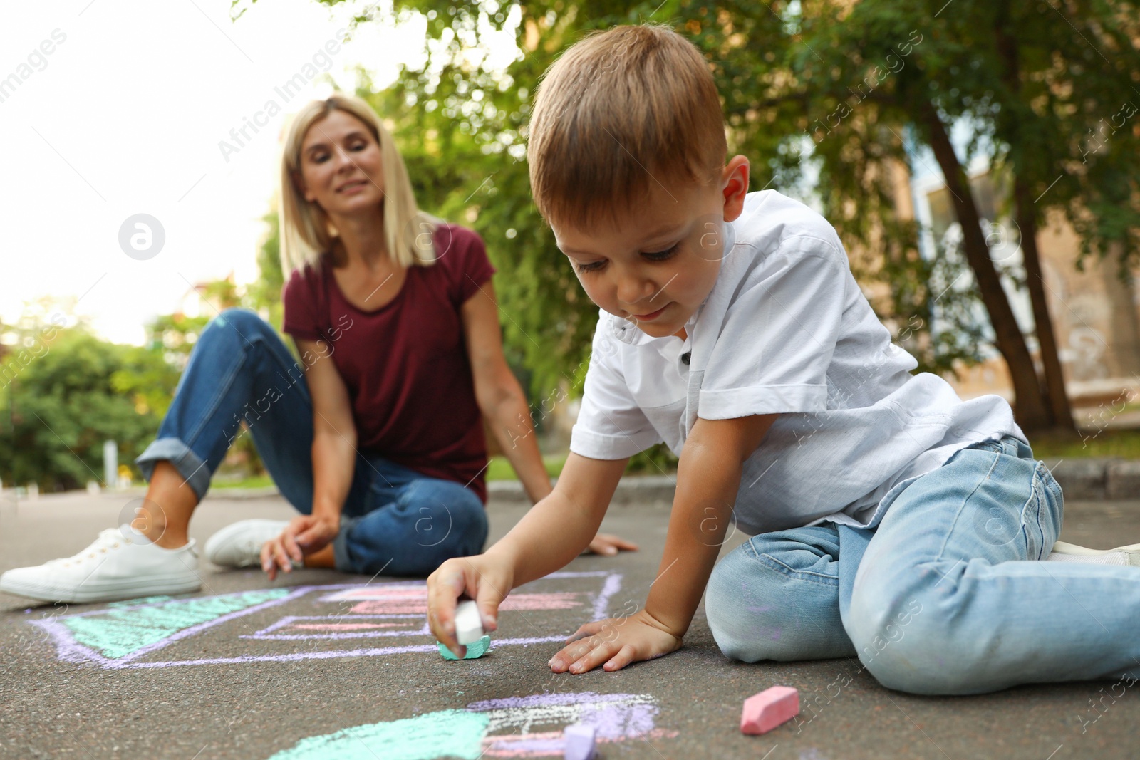 Photo of Nanny with cute little boy drawing house with chalks on asphalt