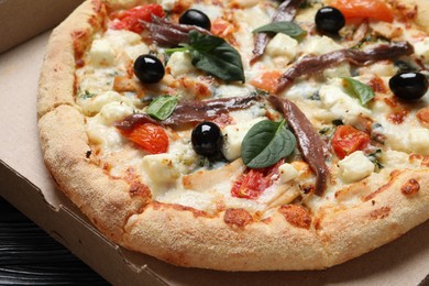 Photo of Tasty pizza with anchovies, basil and olives in cardboard box, closeup