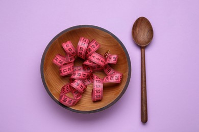 Photo of Measuring tape and wooden spoon on violet background, flat lay. Weight loss concept