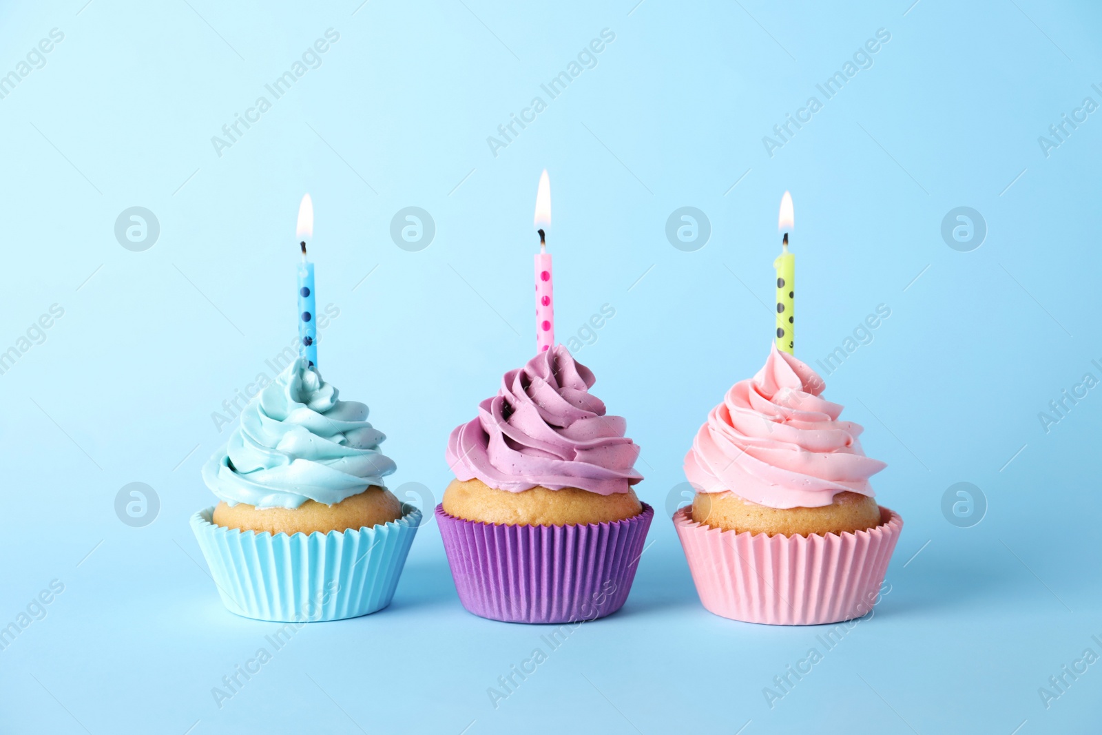 Photo of Delicious birthday cupcakes with burning candles on light blue background