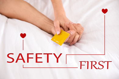 Safety first. Woman and man holding condom together on bed, closeup
