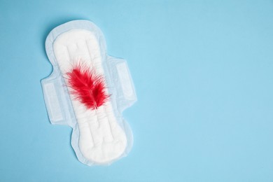 Photo of Menstrual pad with red feather on light blue background, top view. Space for text