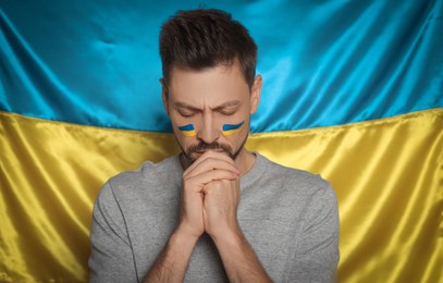 Photo of Sad man with clasped hands near Ukrainian flag