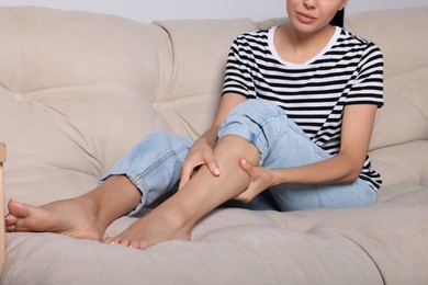 Photo of Young woman rubbing sore leg on sofa, closeup