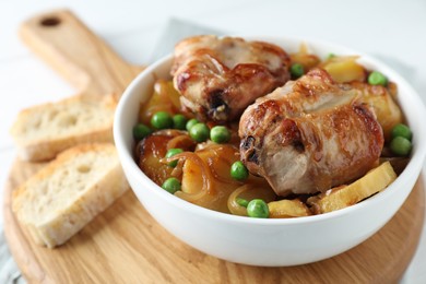 Photo of Tasty cooked rabbit with vegetables in bowl and bread on wooden board, closeup
