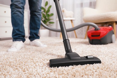 Photo of Man cleaning carpet with vacuum cleaner at home, closeup