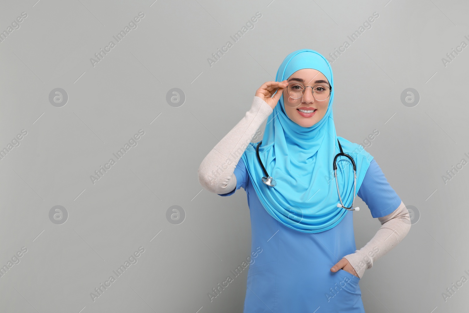 Photo of Muslim woman wearing hijab and medical uniform with stethoscope on light gray background, space for text