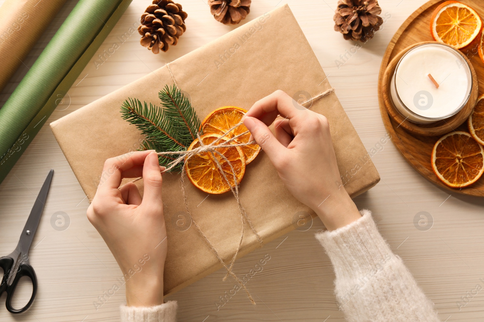 Photo of Woman decorating gift box with dry orange slices at white wooden table, top view