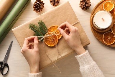 Woman decorating gift box with dry orange slices at white wooden table, top view