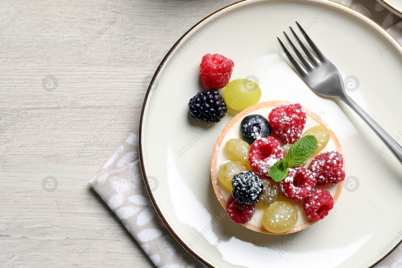 Photo of Delicious tartlet with berries on light wooden table, top view