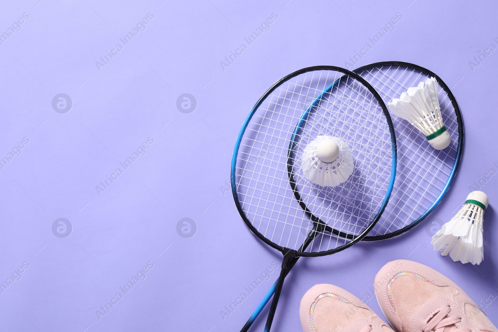 Photo of Feather badminton shuttlecocks, rackets and sneakers on violet background, flat lay. Space for text