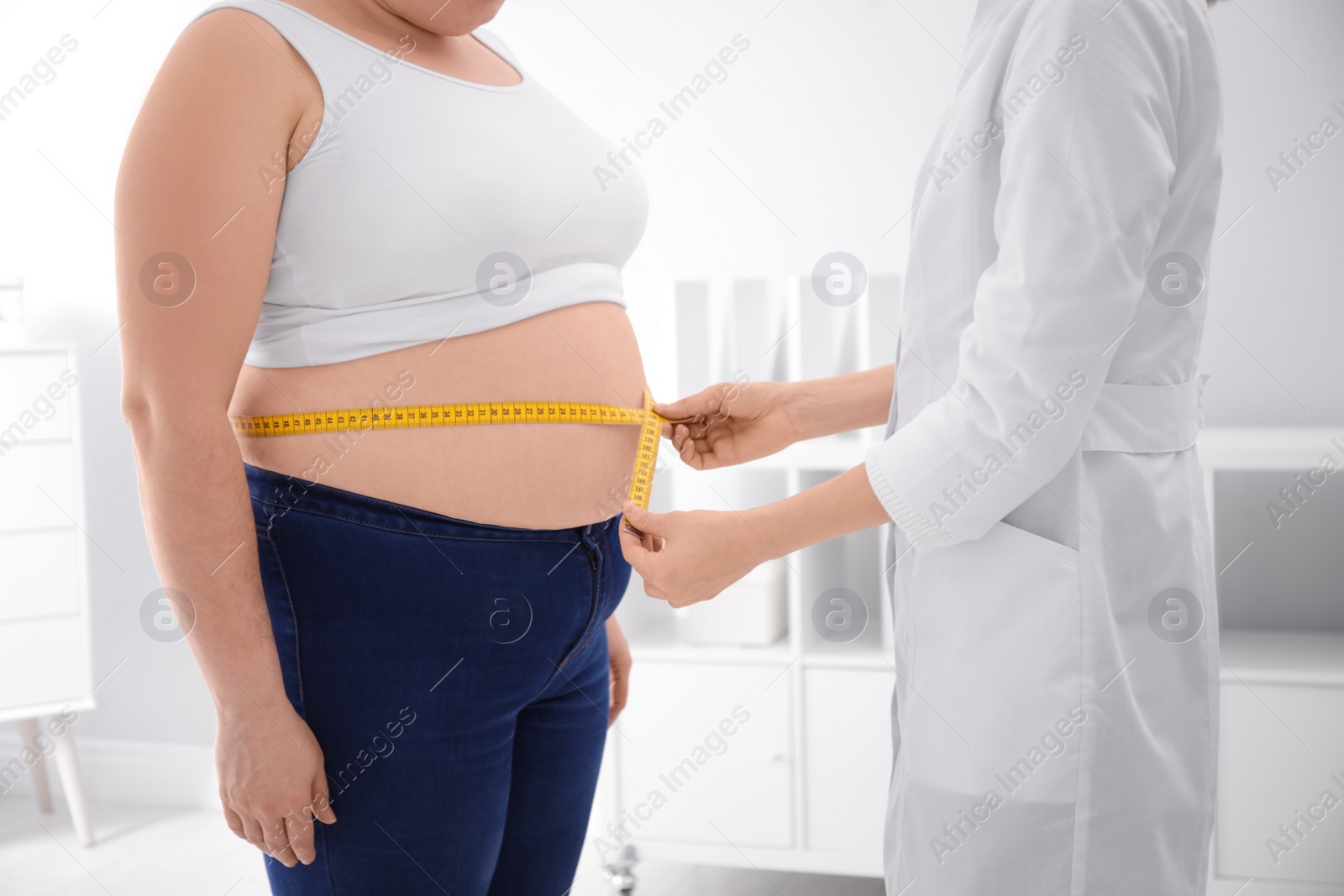 Photo of Doctor measuring waist of overweight woman in clinic, closeup