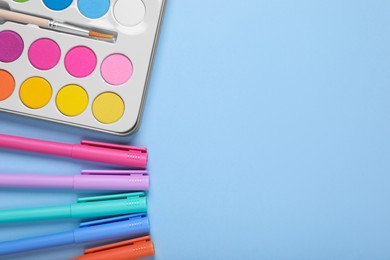 Photo of Watercolor palette with brush and colorful markers on light blue background, flat lay. Space for text