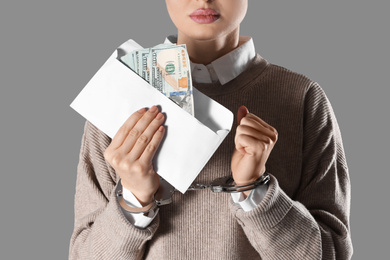 Woman in handcuffs holding bribe money on grey background, closeup
