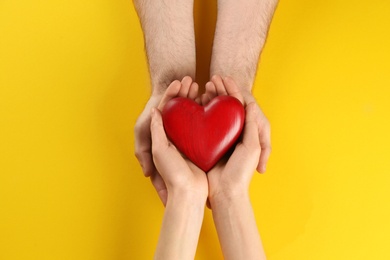 Photo of Couple holding decorative heart on color background, top view